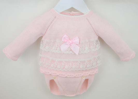 Pink baby outfit with lace details and a bow on a light gray background