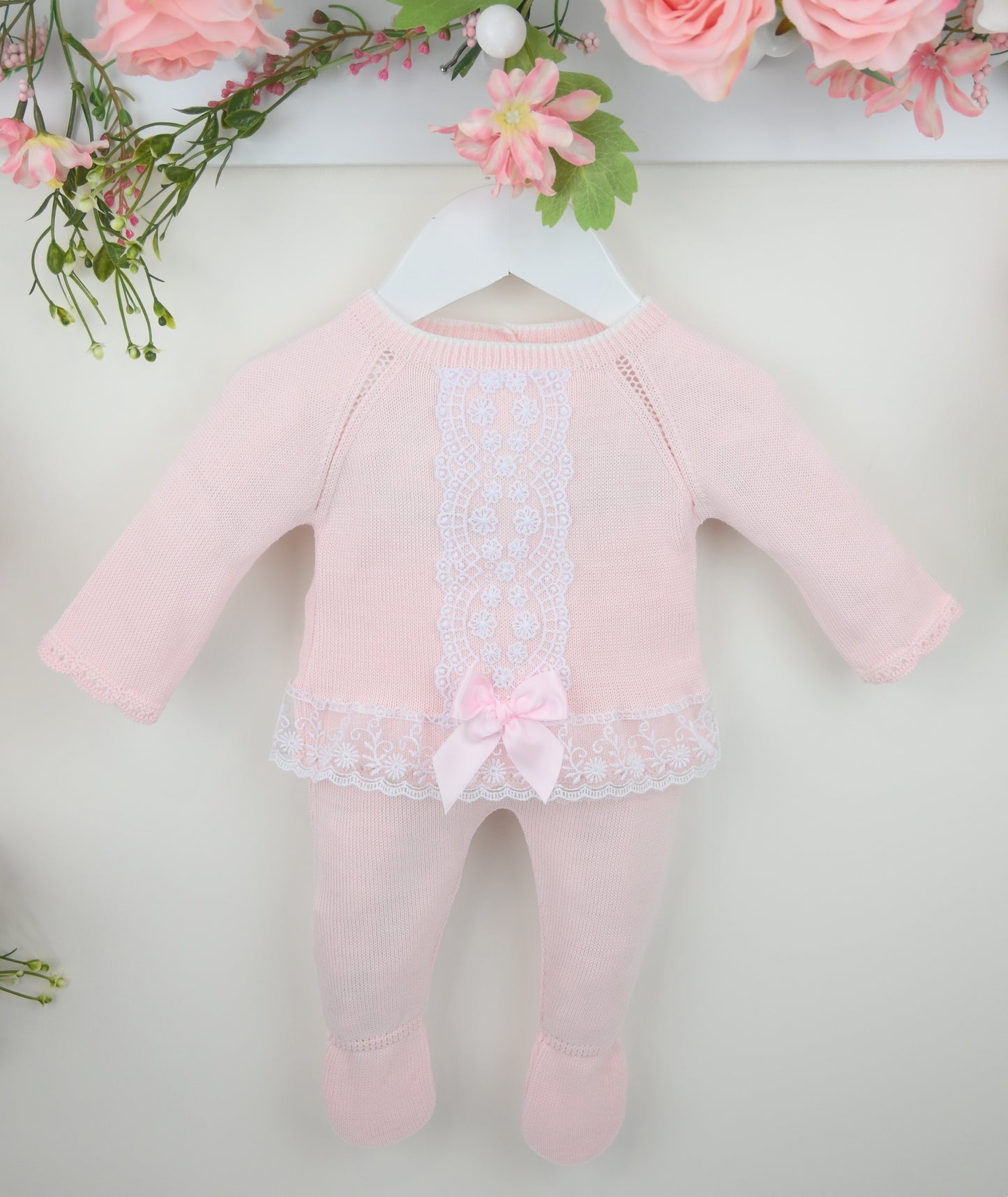 Pink baby romper with lace details on a white background with floral decorations.