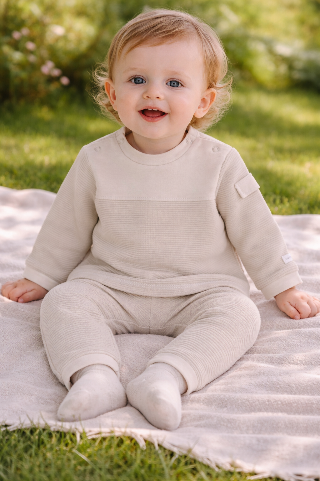 Baby in a beige outfit sitting on a blanket outdoors