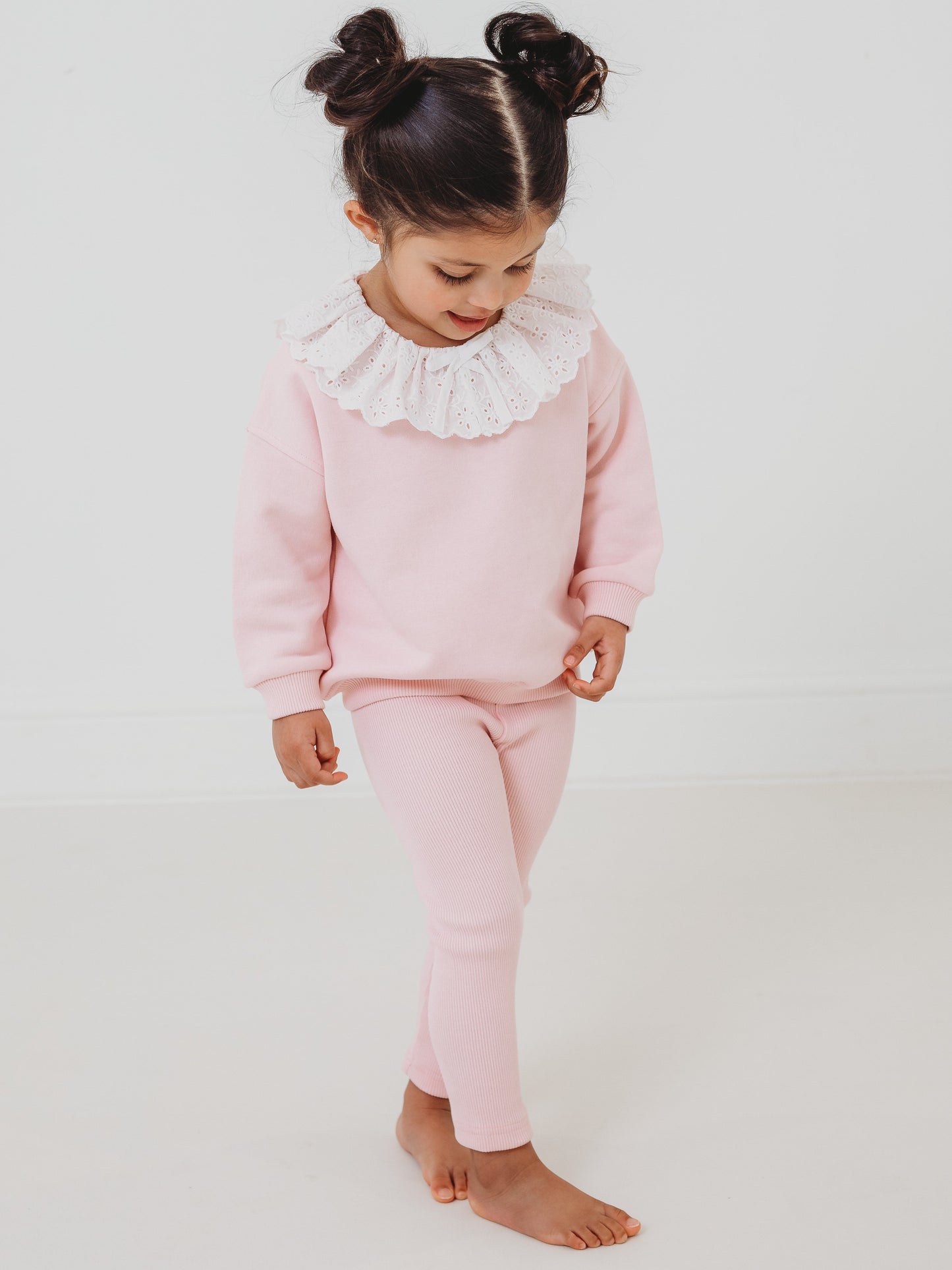 Pink frill-collar anglaise top with ribbed leggings, standing and looking down