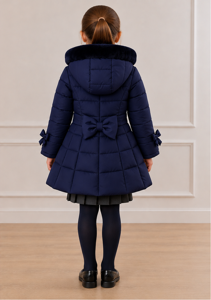 A young girl modeling a navy blue quilted winter coat, shown from both the front and back views against a light-colored paneled wall and wood floor.
