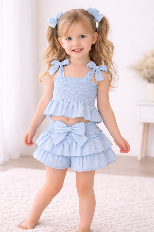 Girl wearing baby pink bow two-piece outfit with smocked top and ruffle shorts for girls
