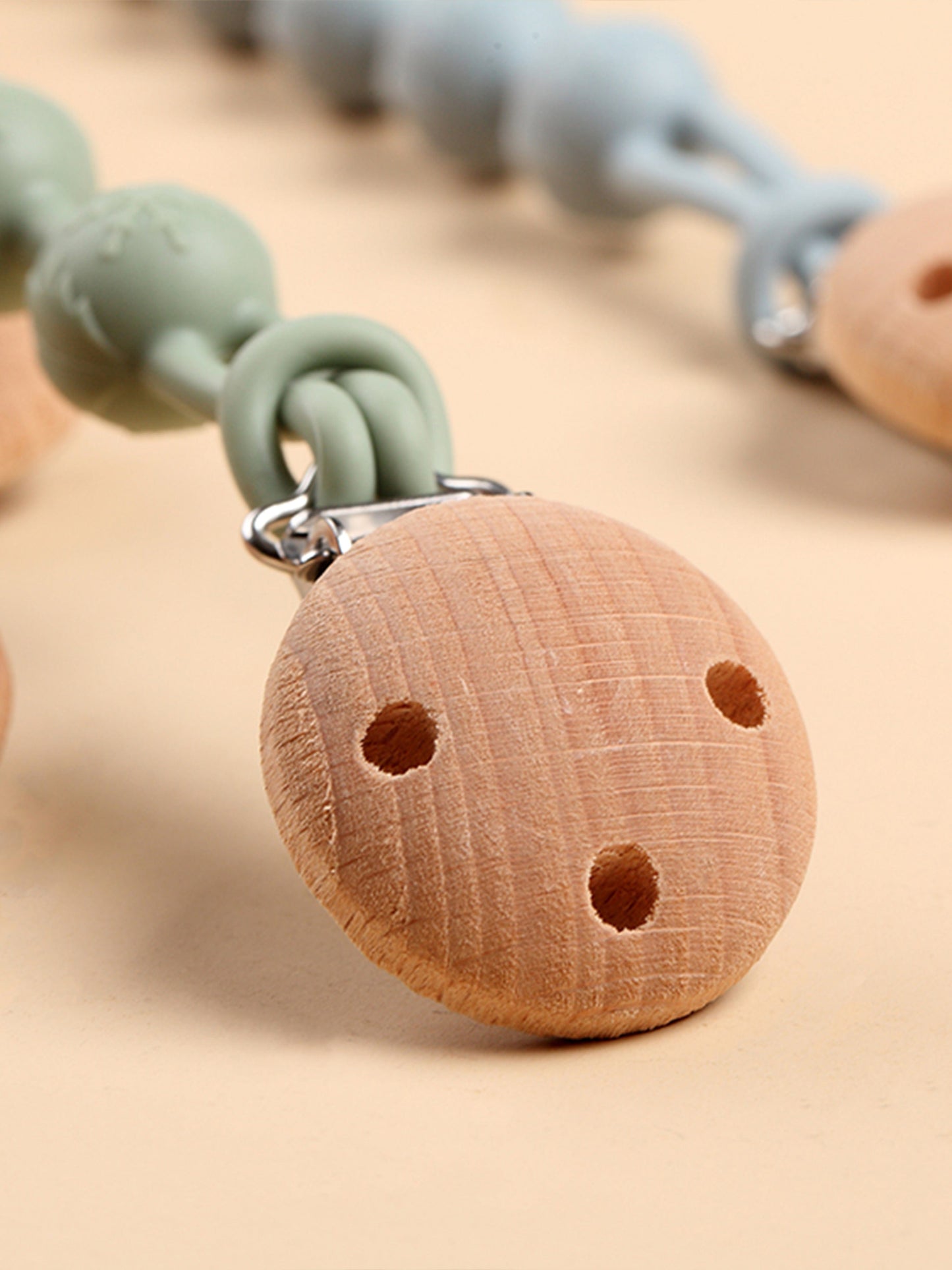 Round wooden teether with two holes, attached by a metal clip on a pale mint strap