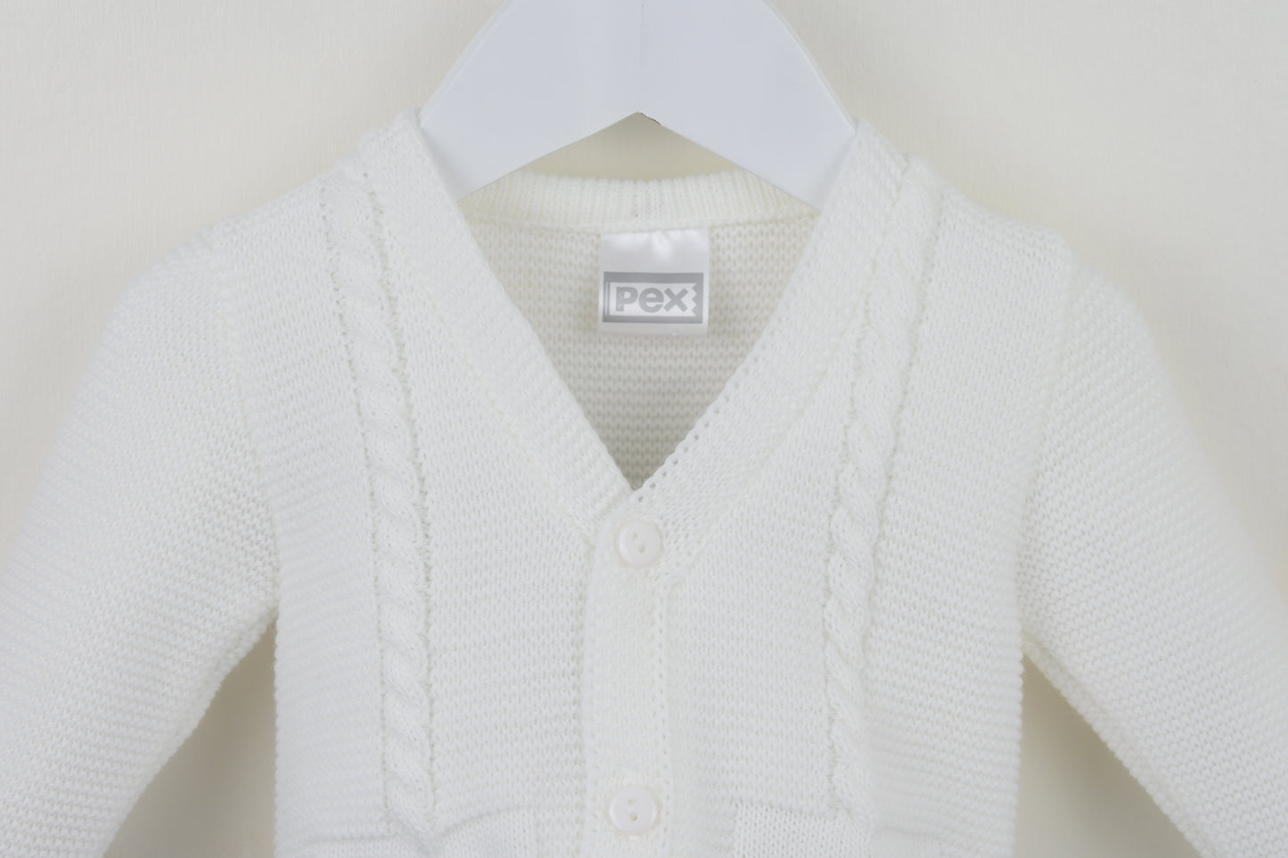 White baby cardigan on a hanger with a visible brand label against a plain background