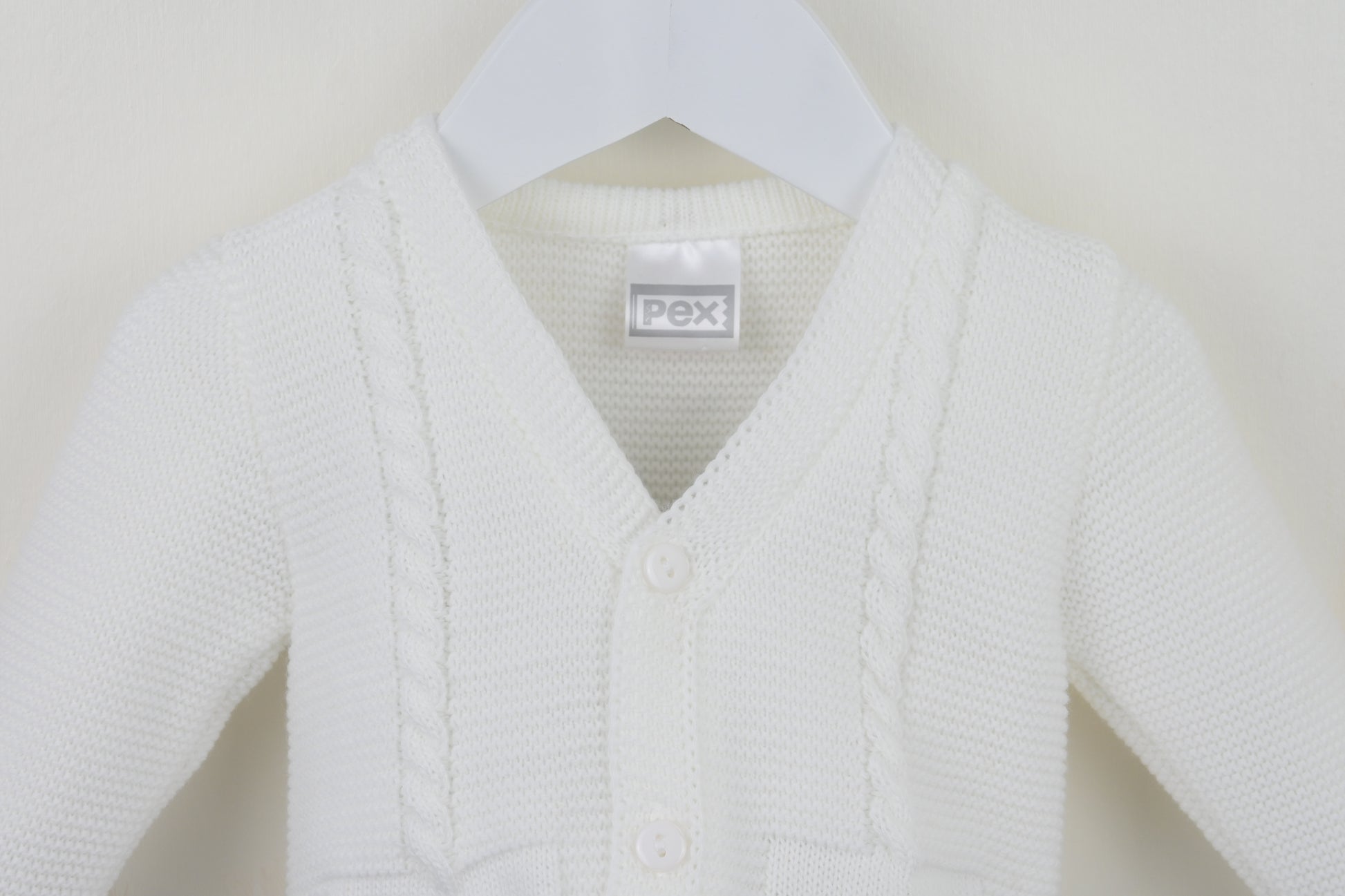 White baby cardigan on a hanger with a visible brand label against a plain background