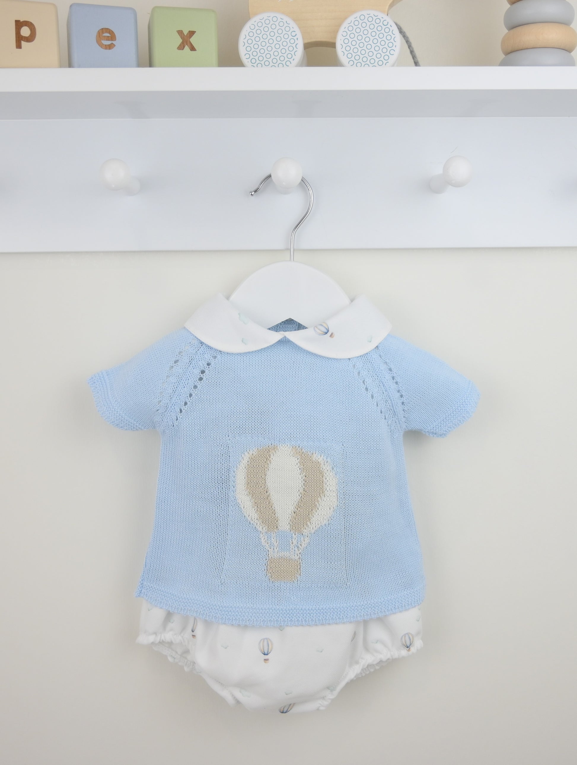 Baby outfit with blue shirt and white diaper on a hanger against a neutral background