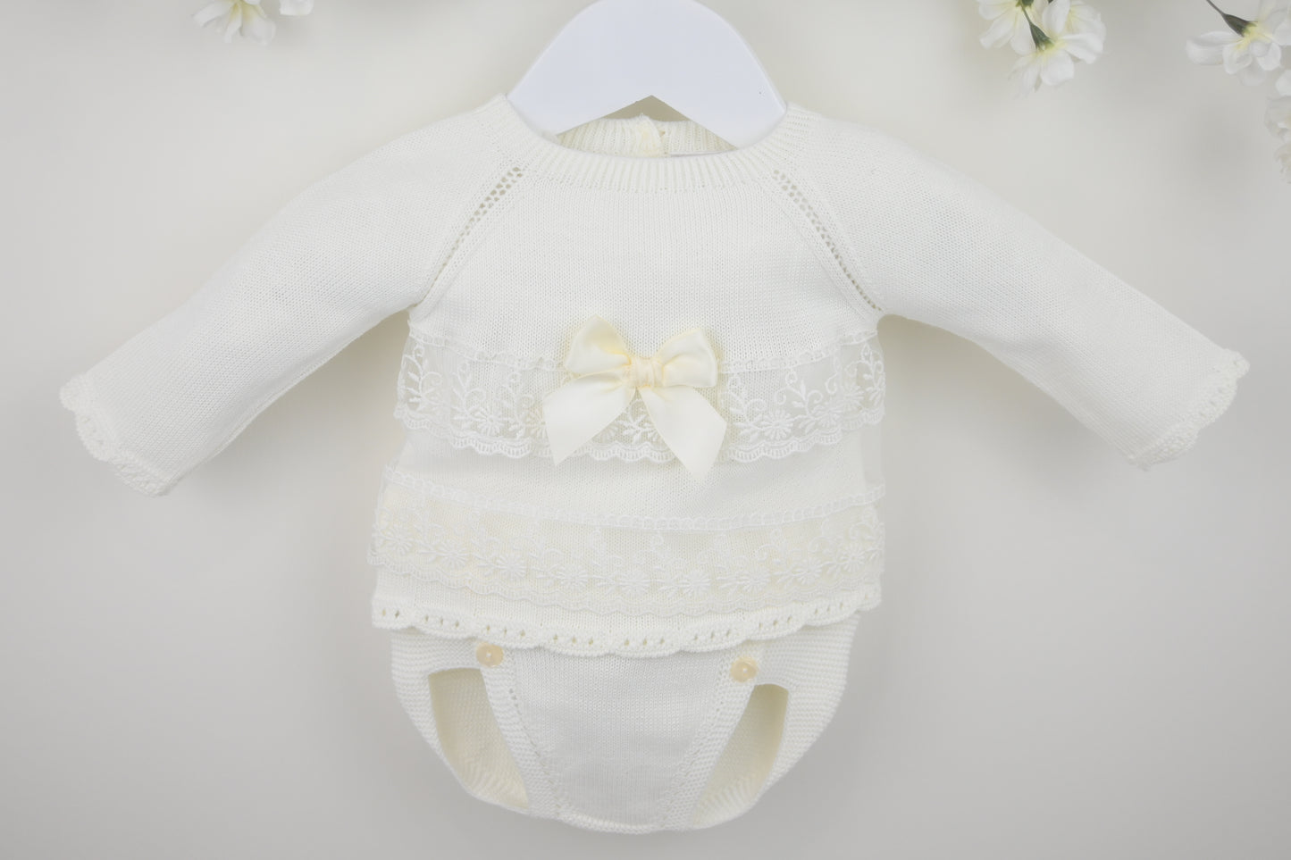 White baby romper with lace details and a bow on a white background