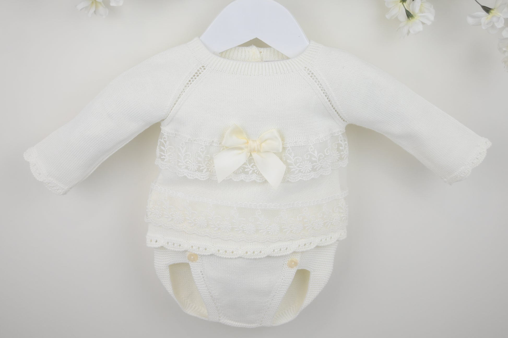 White baby romper with lace details and a bow on a white background