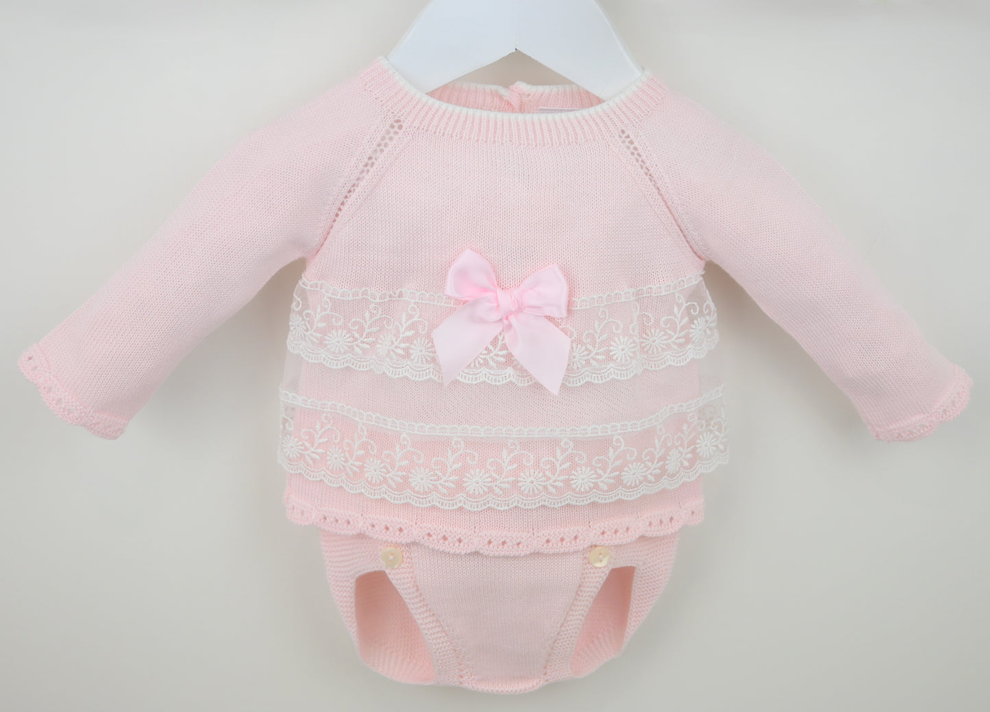 Pink baby outfit with lace details and a bow on a light gray background