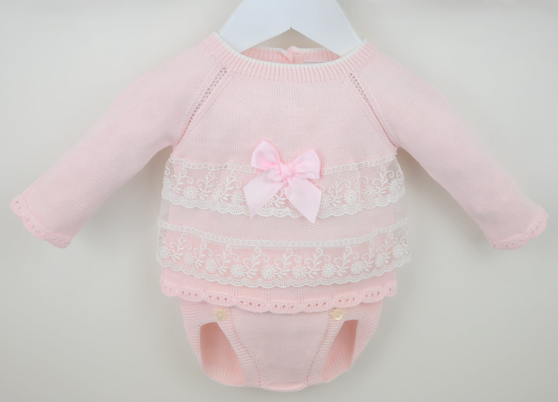 Pink baby outfit with lace details and a bow on a light gray background