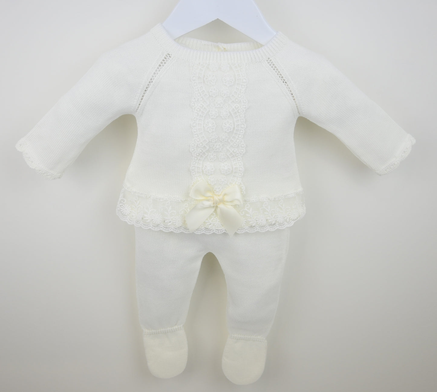 White baby outfit with a lace detail on a plain background