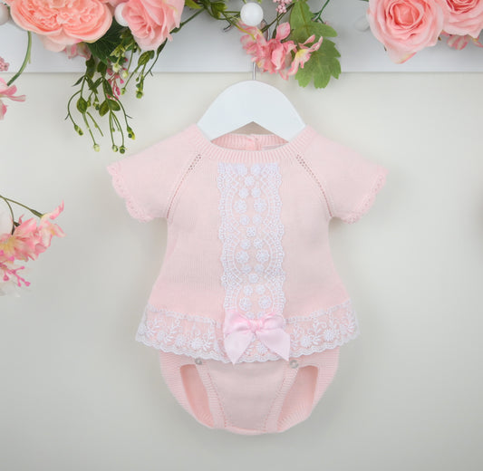 Pink baby romper with lace details on a white background with floral decorations