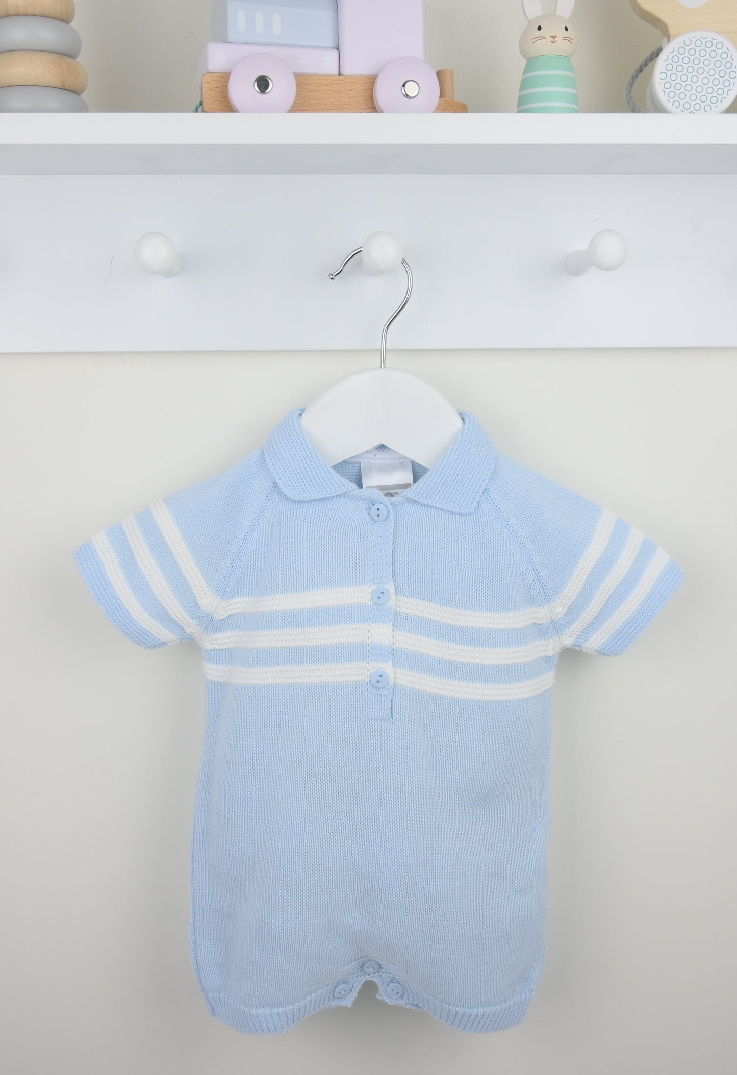 Baby blue knitted romper with white stripes on a hanger against a neutral background.