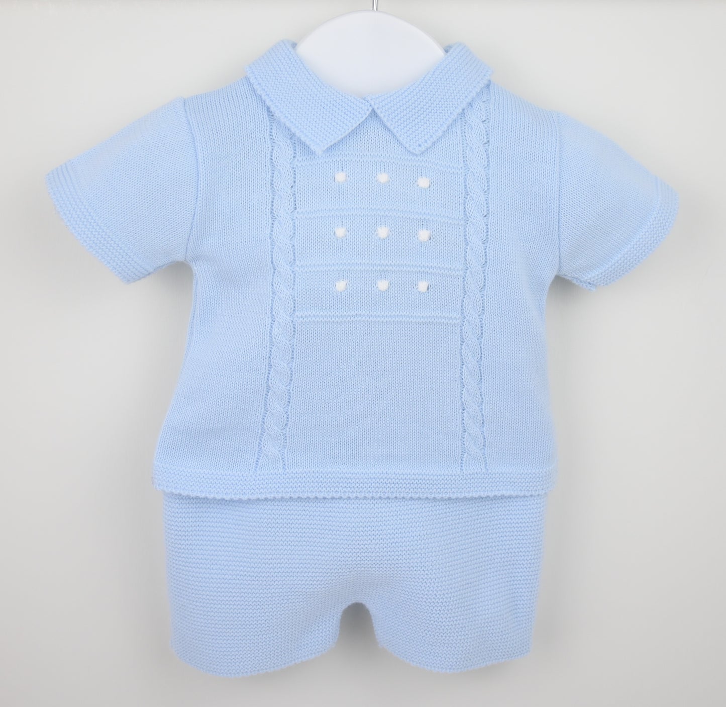 Baby blue knitted shorts suit with collar and cable detail displayed on hanger