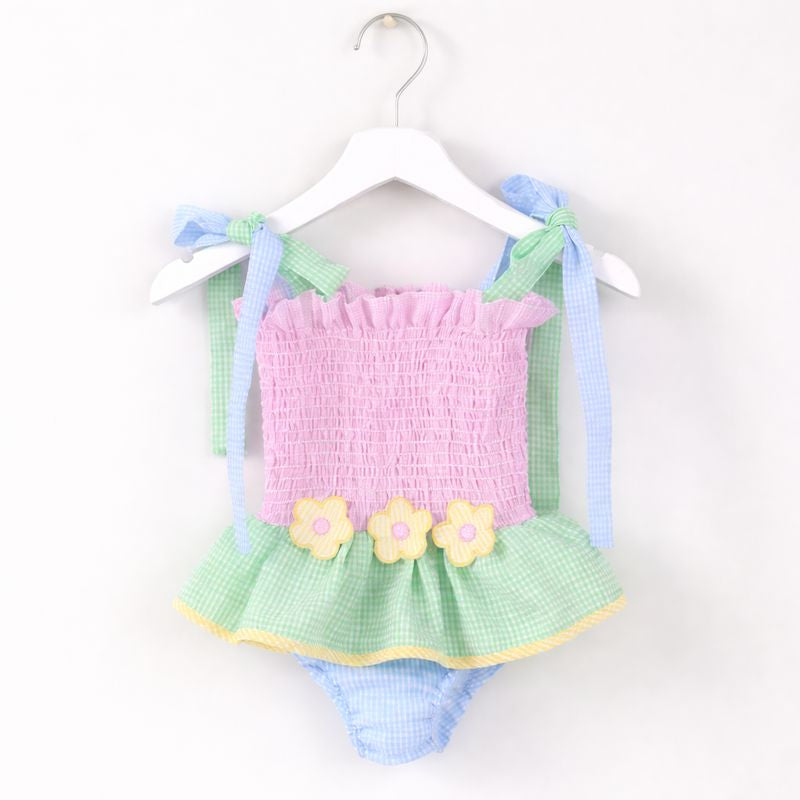 Pastel baby outfit with pink top and green checkered skirt on a hanger against a white background