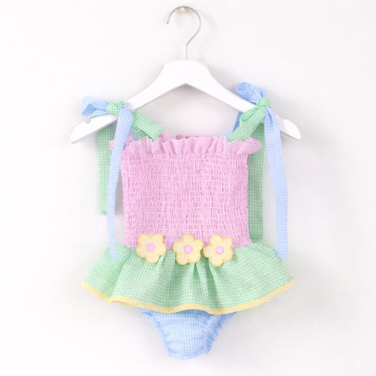 Pastel baby outfit with pink top and green checkered skirt on a hanger against a white background