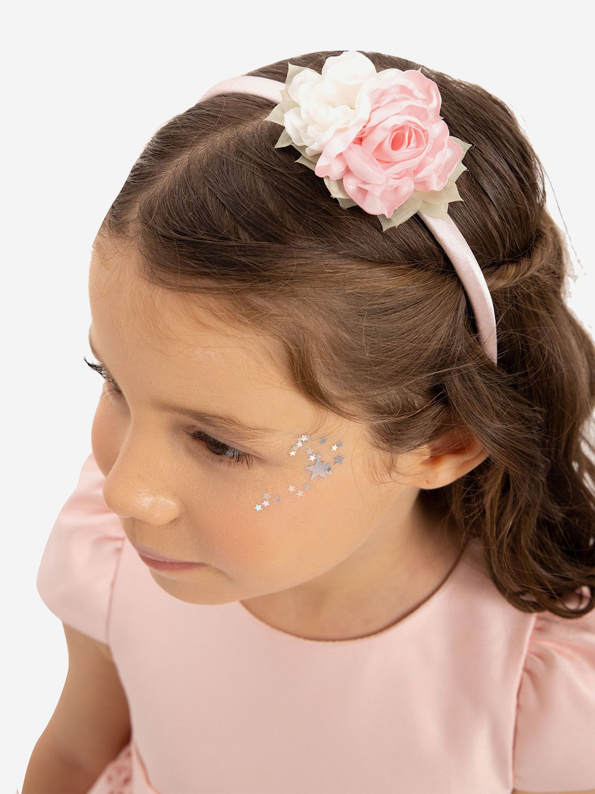 Pink headband with layered fabric flowers; matching pink dress shoulder visible