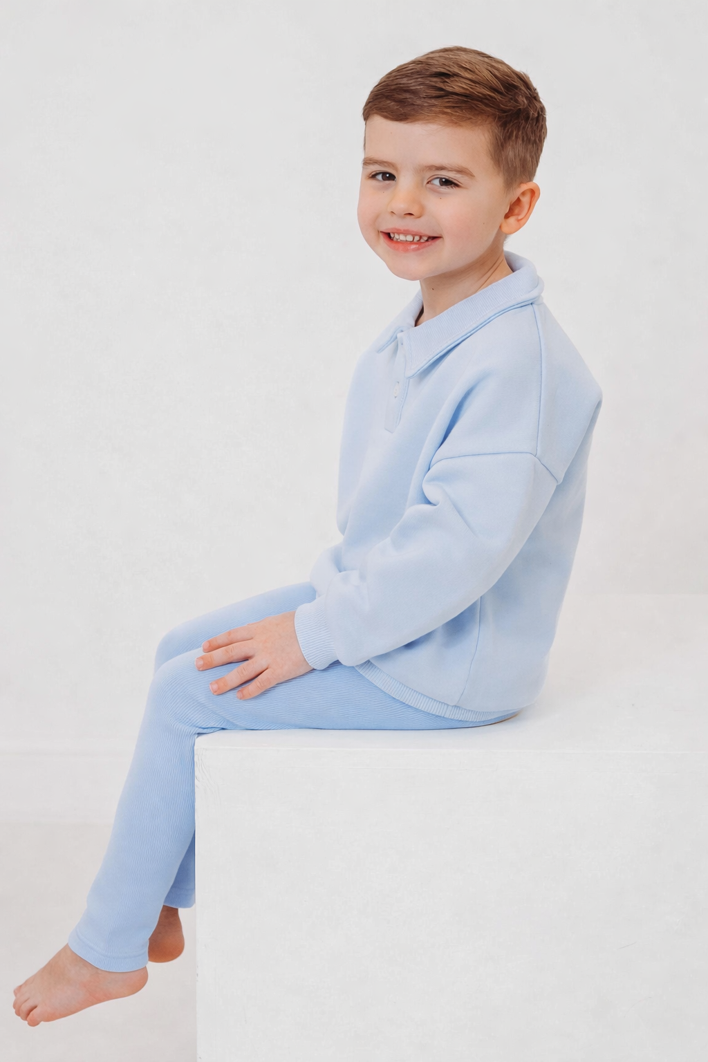 Light blue polo collar top and ribbed leggings set, side view seated on block