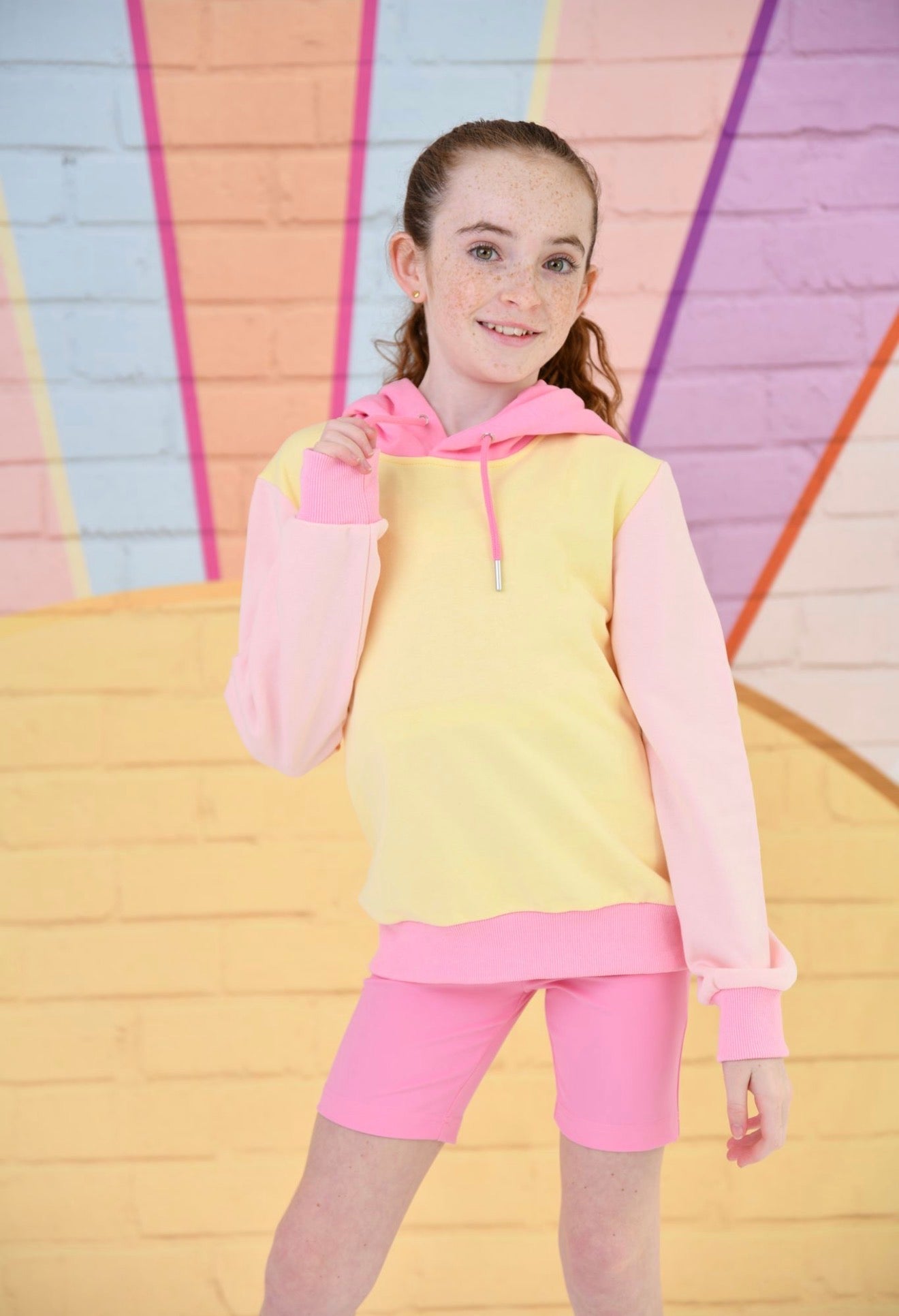 Young girl wearing a pink and yellow outfit with a colorful geometric background