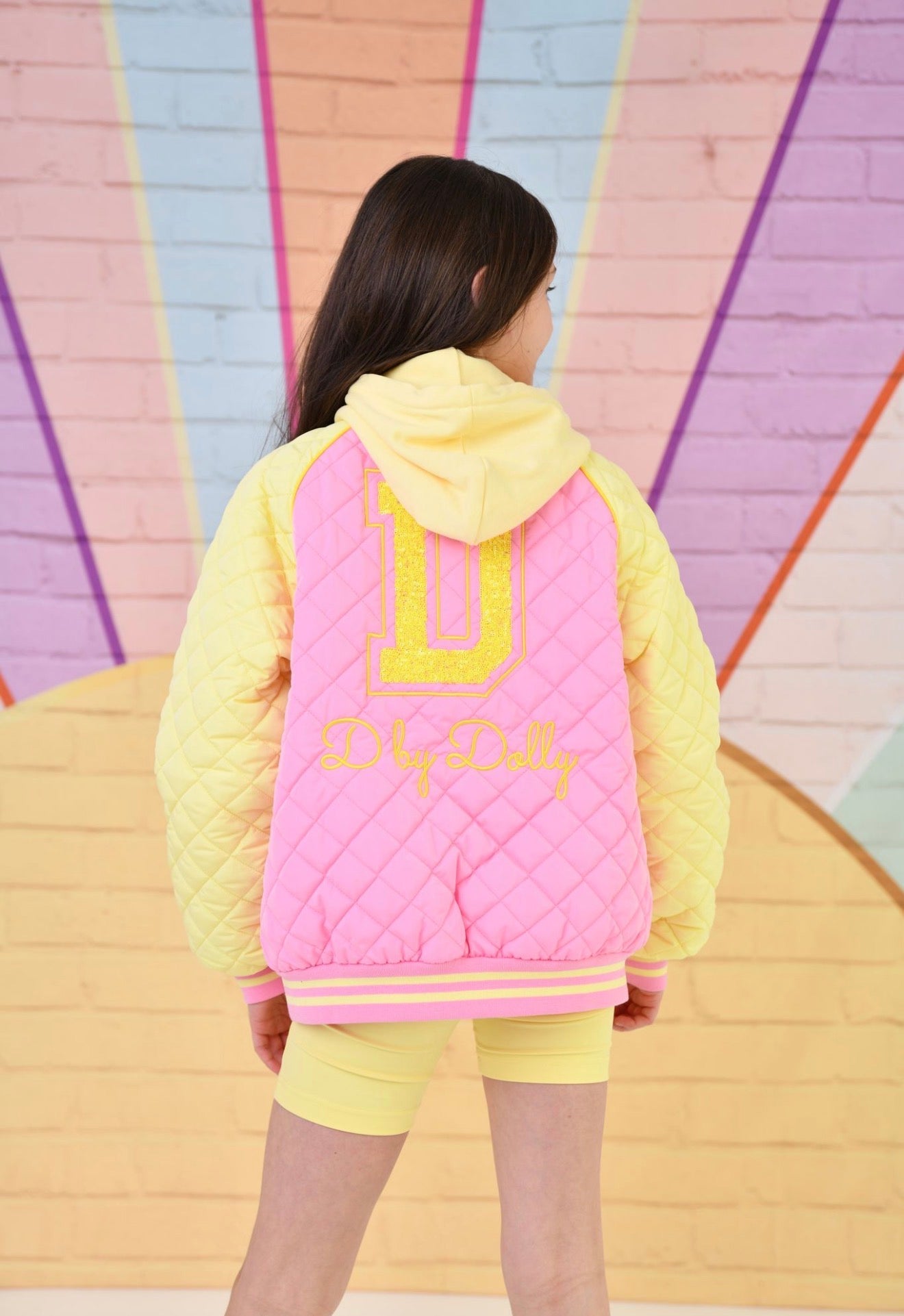 Kids quilted bomber jacket, yellow sleeves and bright pink body, back view with hood