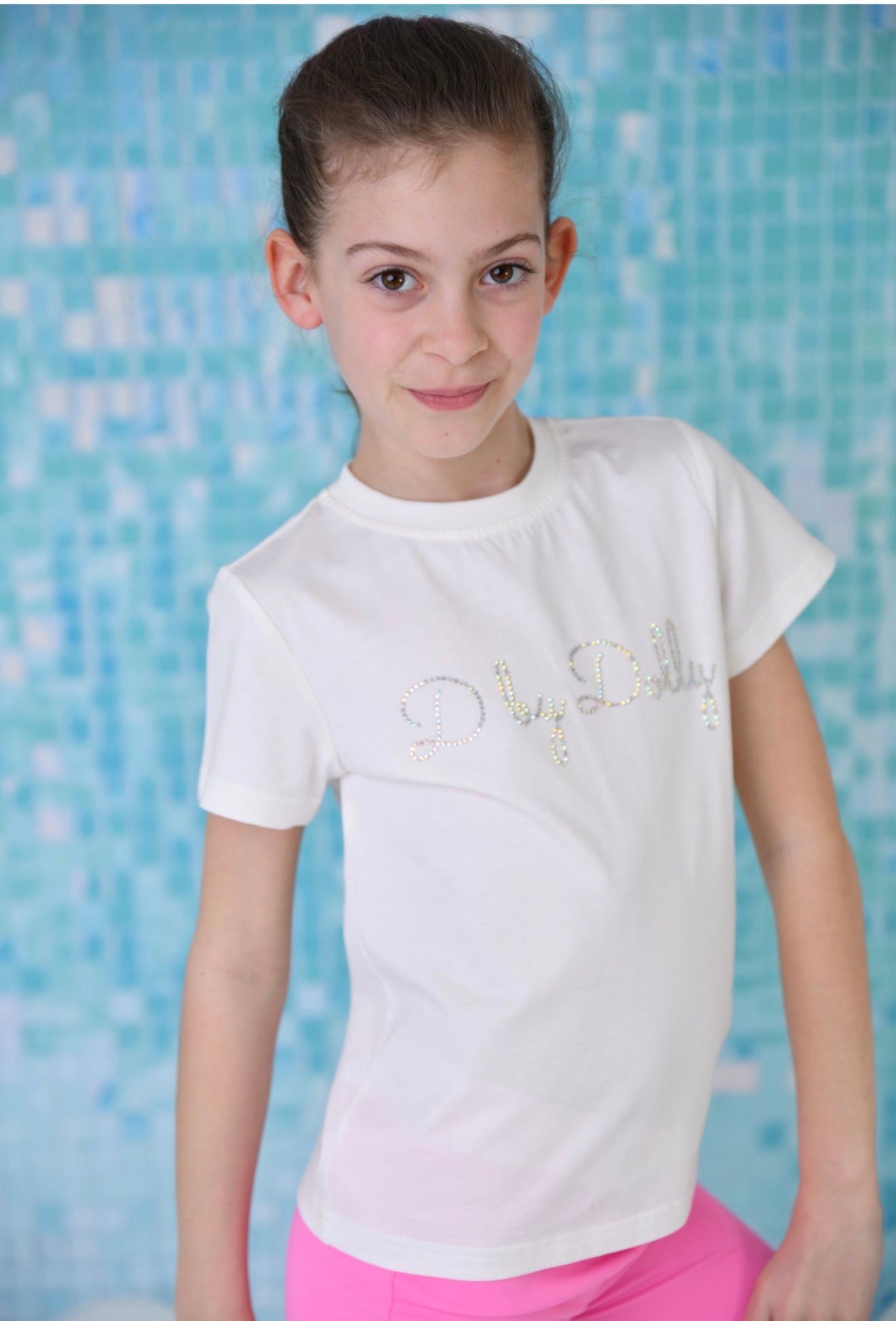 Young girl wearing a white t-shirt with decorative elements against a blue tiled background