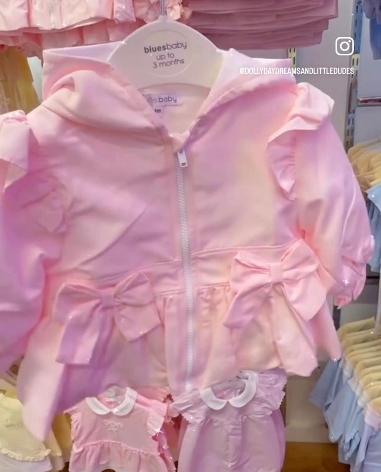 Pink baby jacket with ruffles and a bow on a hanger.
