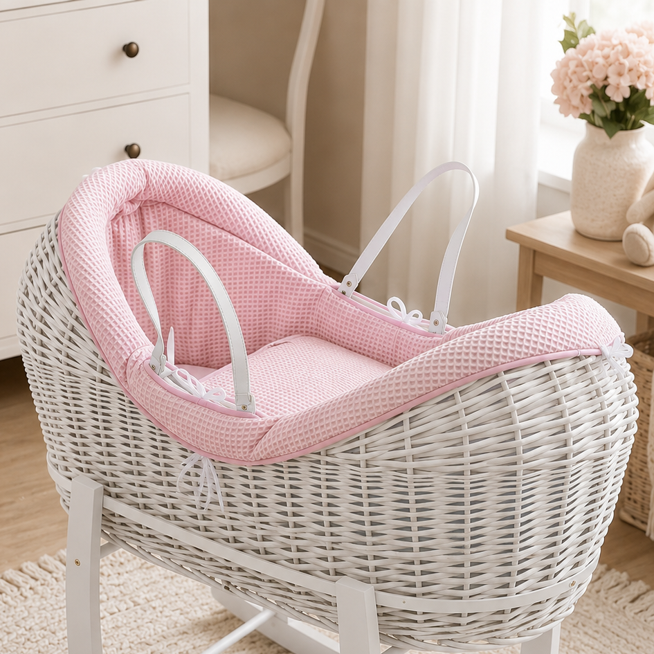 Pink wicker baby moses basket with waffle-textured bedding and white carry handles