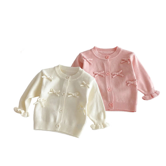 Two baby cardigans, one white and one pink, with bow details on a light gray background.