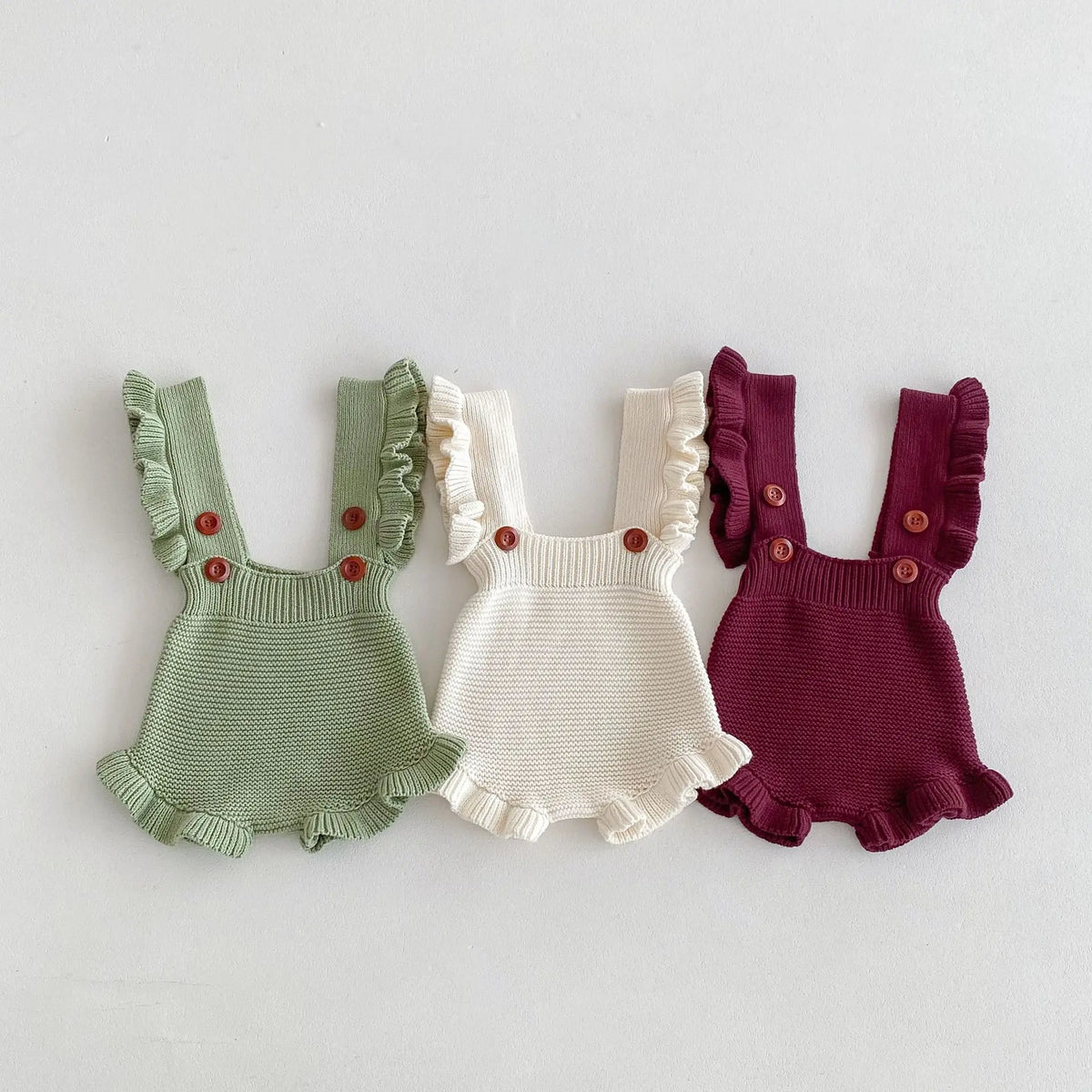 Three baby knit rompers, flat lay—green, cream, and burgundy with ruffled shoulder bibs