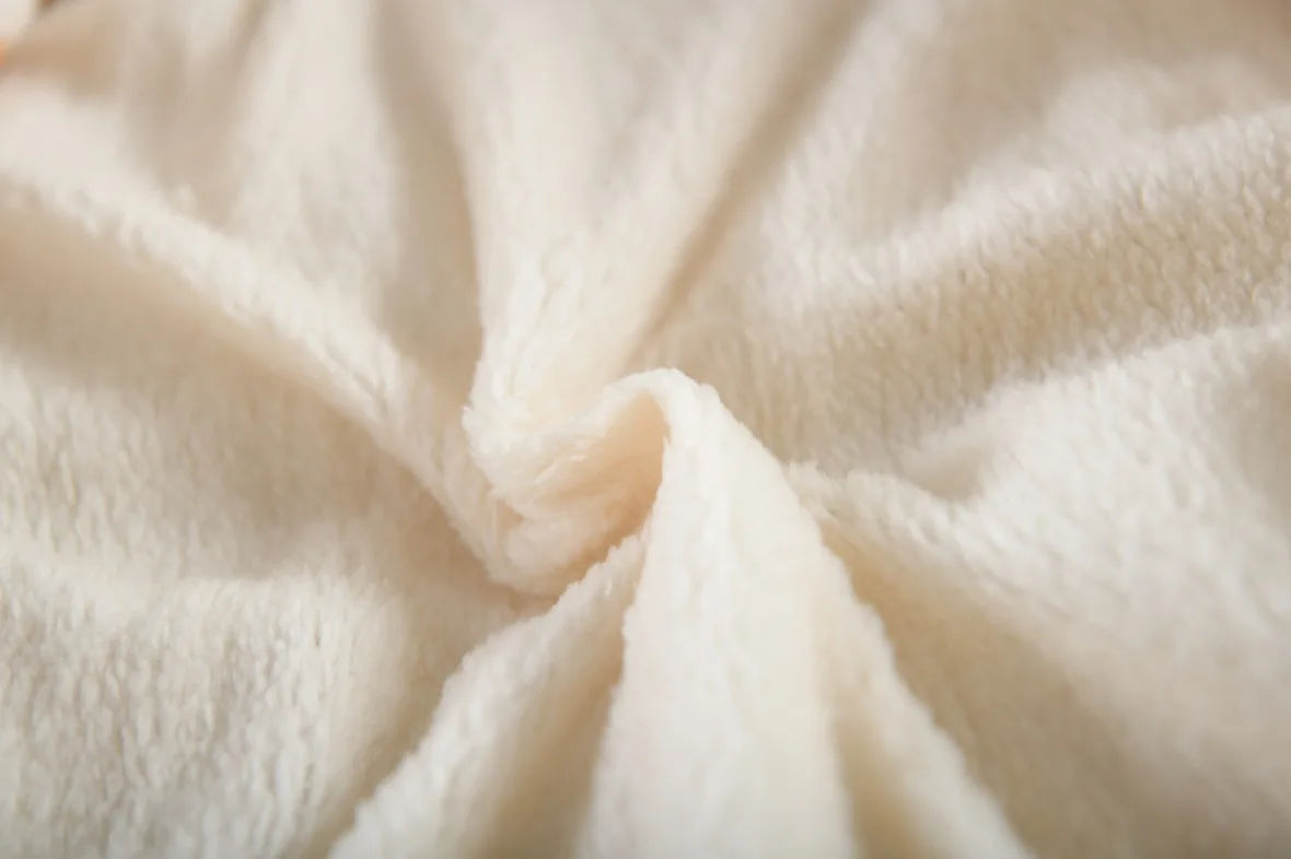 A close-up of soft, plush cream-colored fabric with a textured sherpa or fleece surface, gathered in the center to show the material's depth and softness.