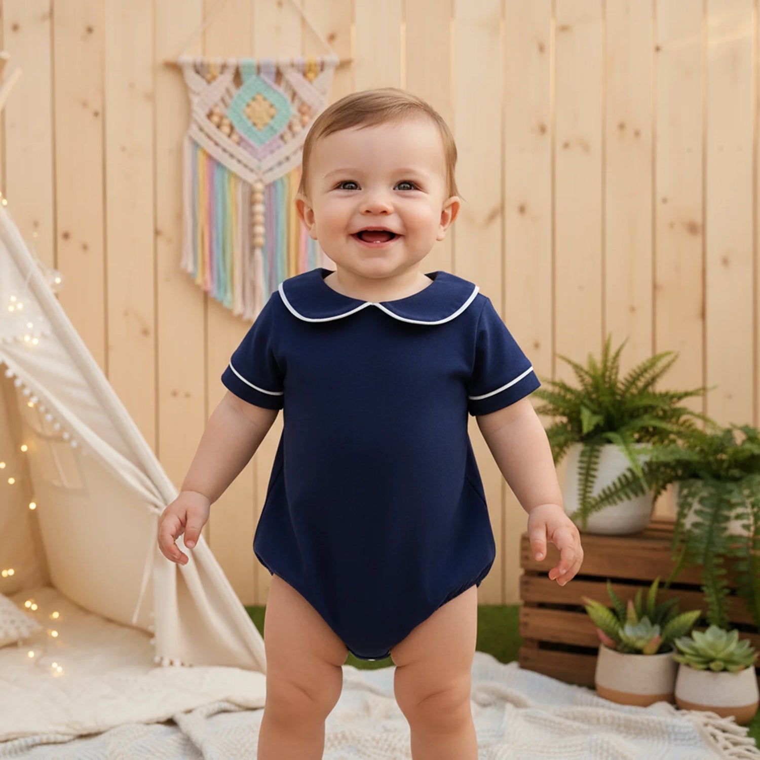 Baby wearing a navy blue onesie with a white collar in an outdoor setting.