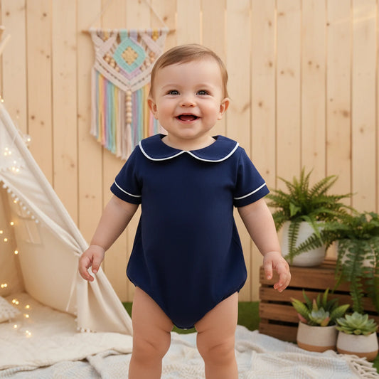 Baby wearing a navy blue onesie with a white collar in an outdoor setting.