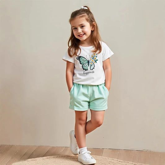 Young girl wearing a white t-shirt with a butterfly design and light green shorts on a plain background
