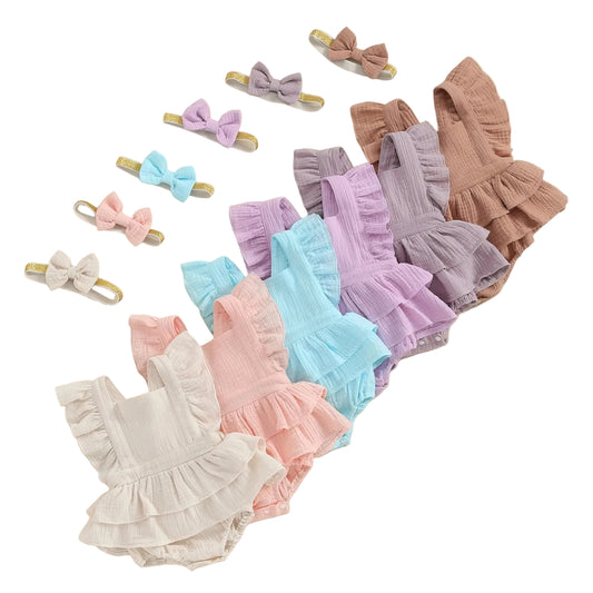 Pastel-colored baby rompers and hair bows arranged on a beige background with green leaves.