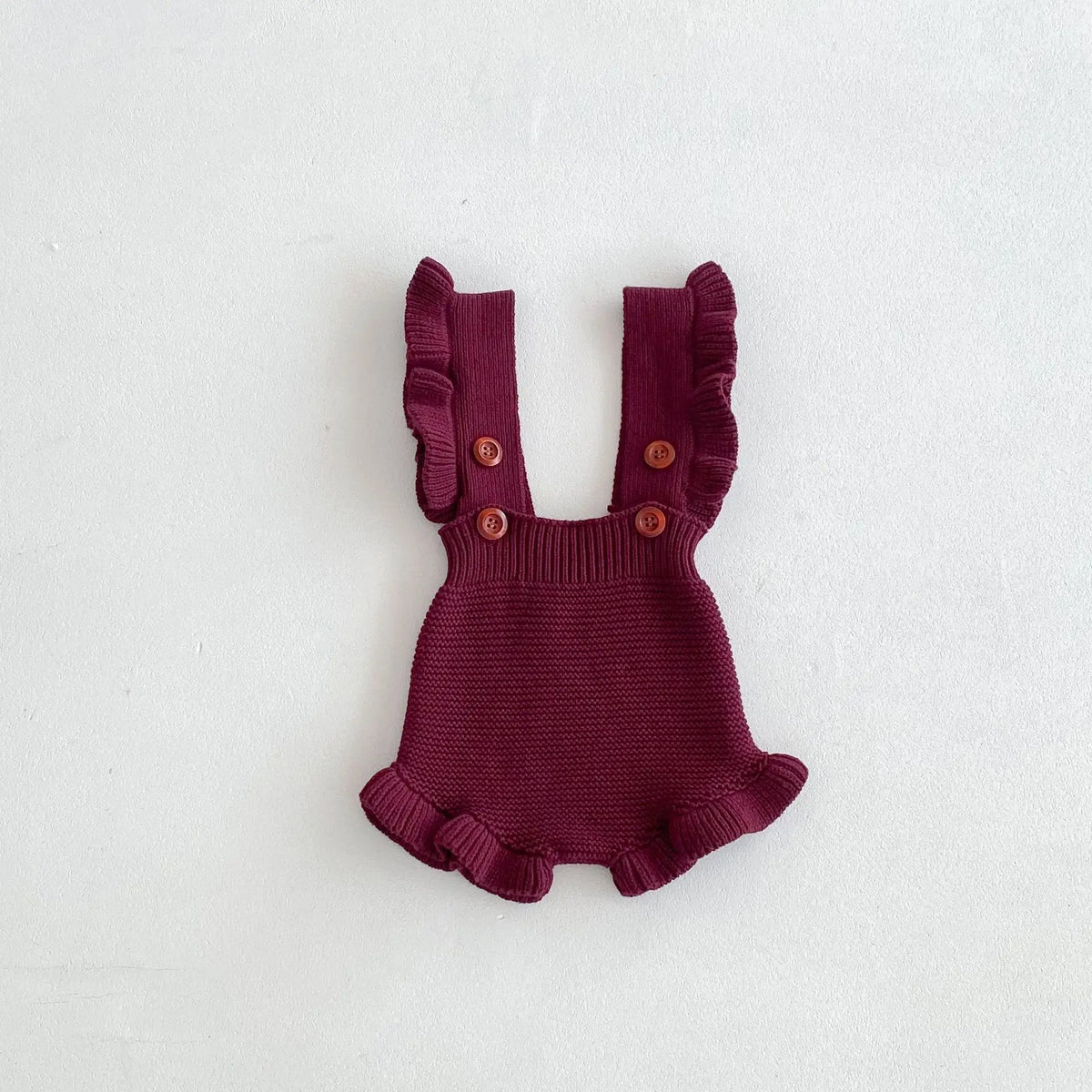 Burgundy baby knit romper close-up with ruffled arm openings and button straps