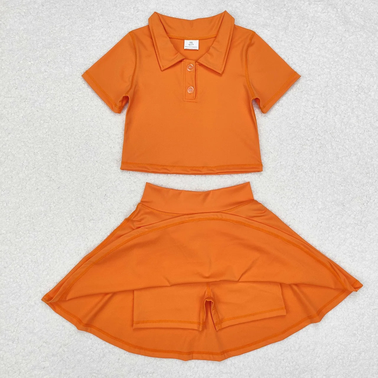 Orange children's shirt and skirt set on a textured white background