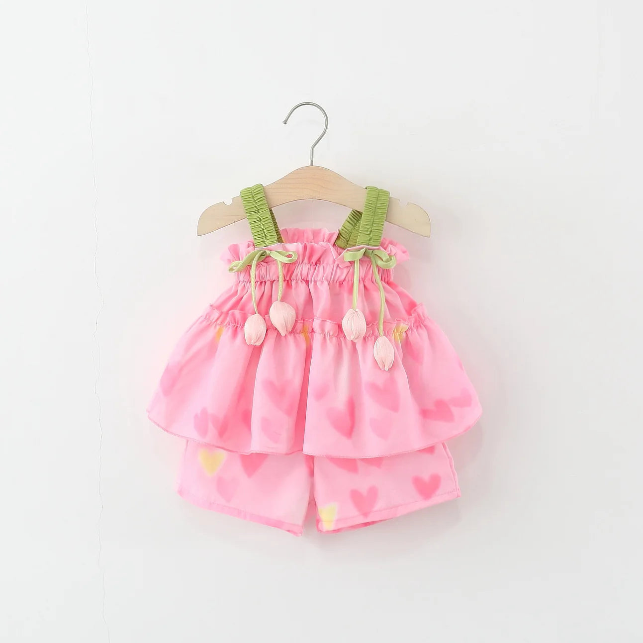 Pink baby dress with green straps on a white background