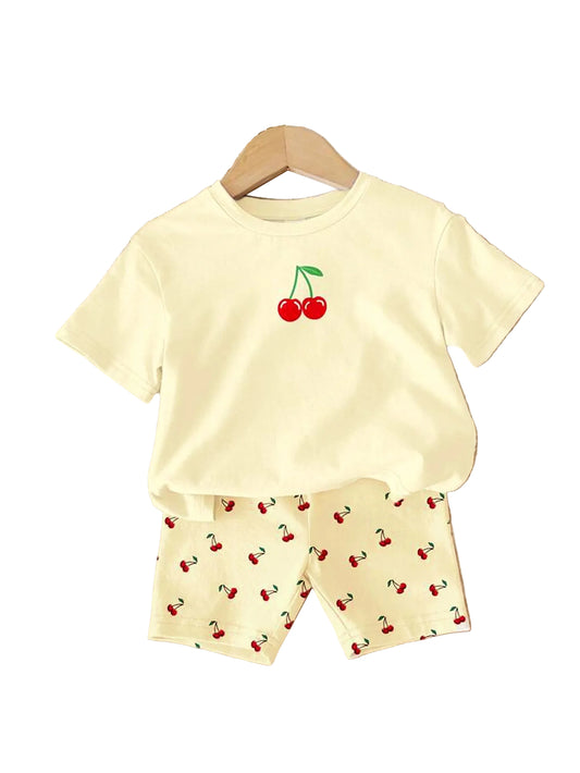 Children's outfit with yellow t-shirt and shorts featuring cherry designs on a wooden surface.