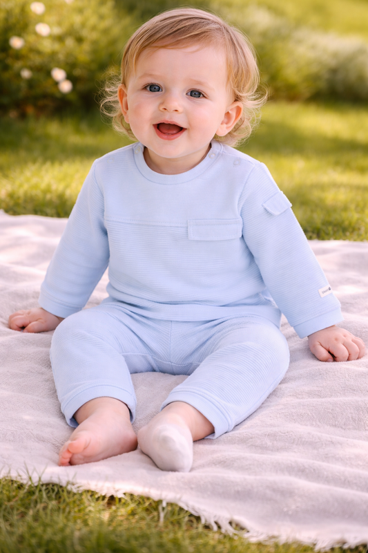 Baby in a light blue outfit sitting on a blanket outdoors.