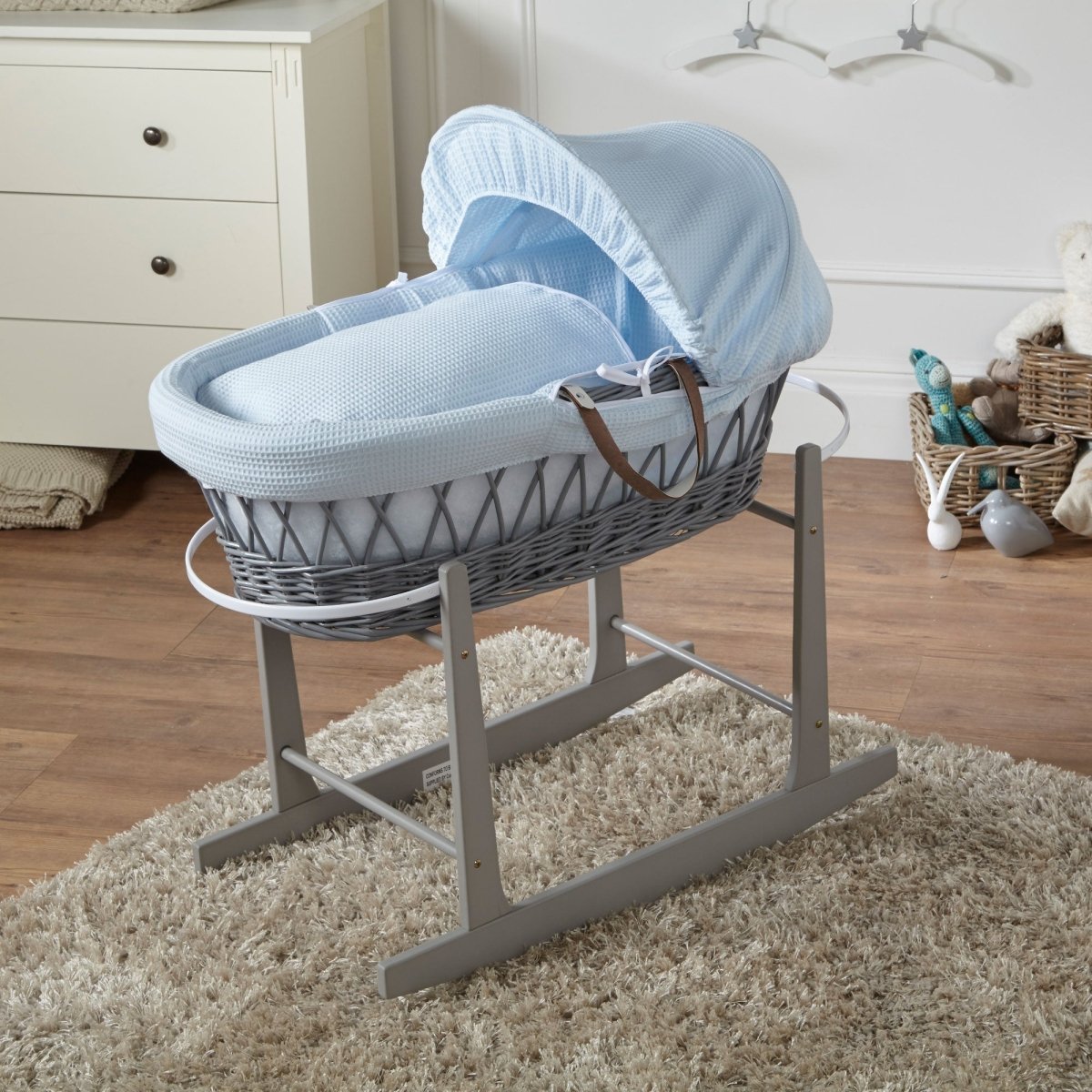 Grey wicker baby Moses basket with blue canopy and padded mattress on grey stand