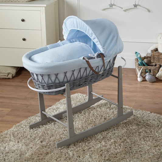 Grey wicker baby Moses basket with blue canopy and padded mattress on grey stand
