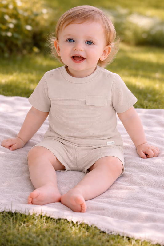 Baby in a beige outfit sitting on a blanket outdoors