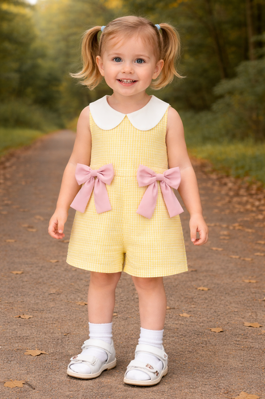 Young girl in a yellow dress with pink bows standing on a path in a natural setting