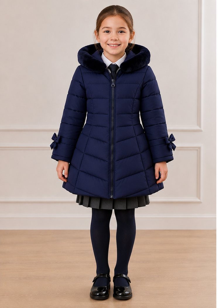 A young girl modeling a navy blue quilted winter coat, shown from both the front and back views against a light-colored paneled wall and wood floor.