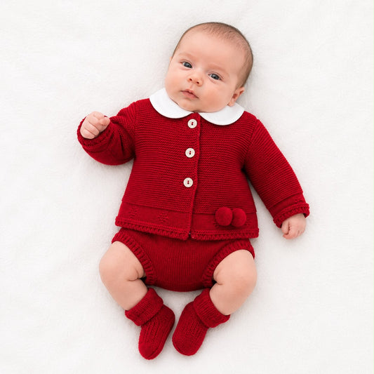 Red knit baby cardigan set with white collar, pom buttons, matching pants and booties