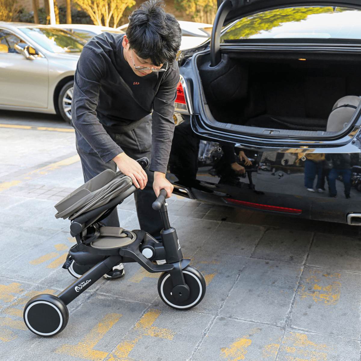 Jet black foldable trike being lifted for transport, with large wheels and seat frame