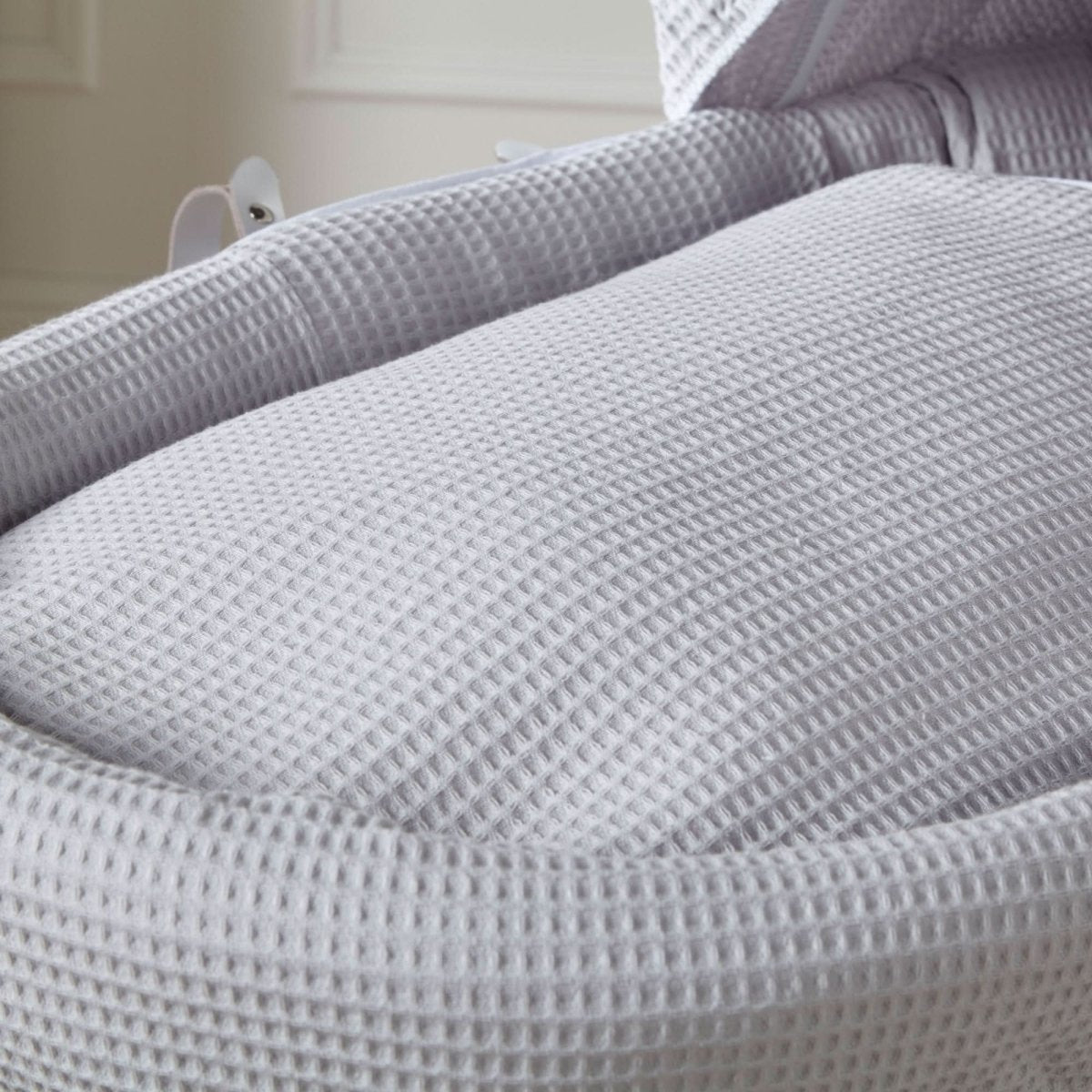 Close-up grey waffle bedding inside Moses basket with padded surround and hood