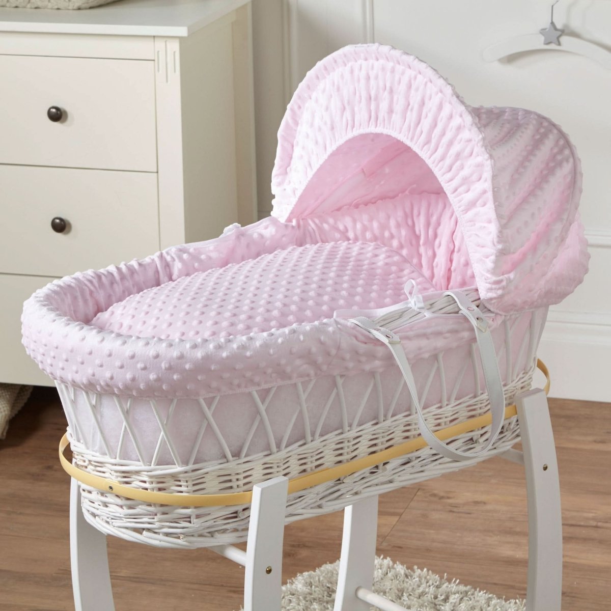 Pink Moses basket on white wicker stand with arched canopy and padded dotted mattress
