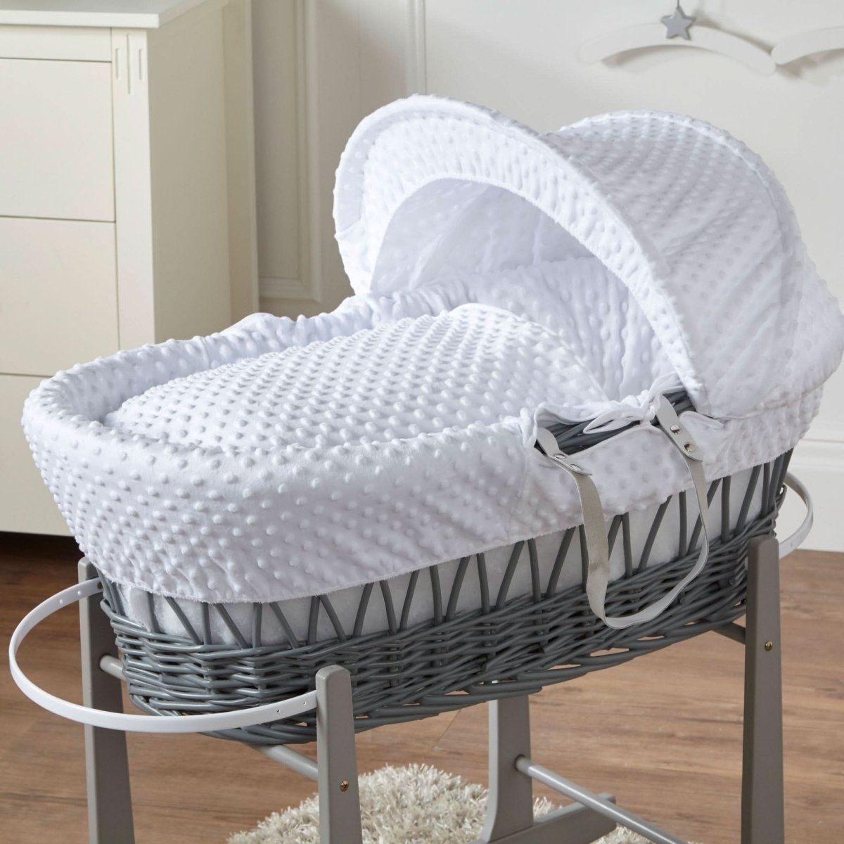 White padded Moses basket on grey wicker stand with fitted hood and tie